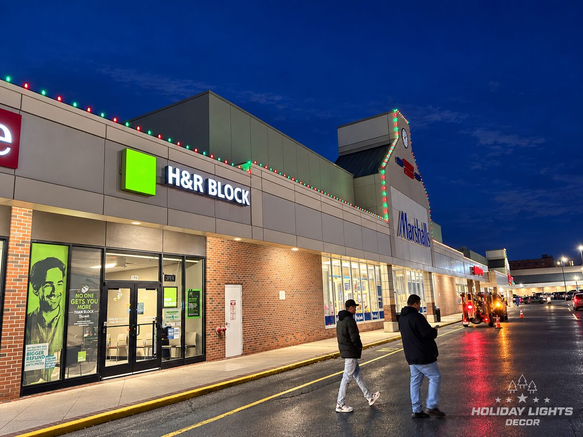 Red and green bulbs follow a long commercial parapet toward a raised tower.