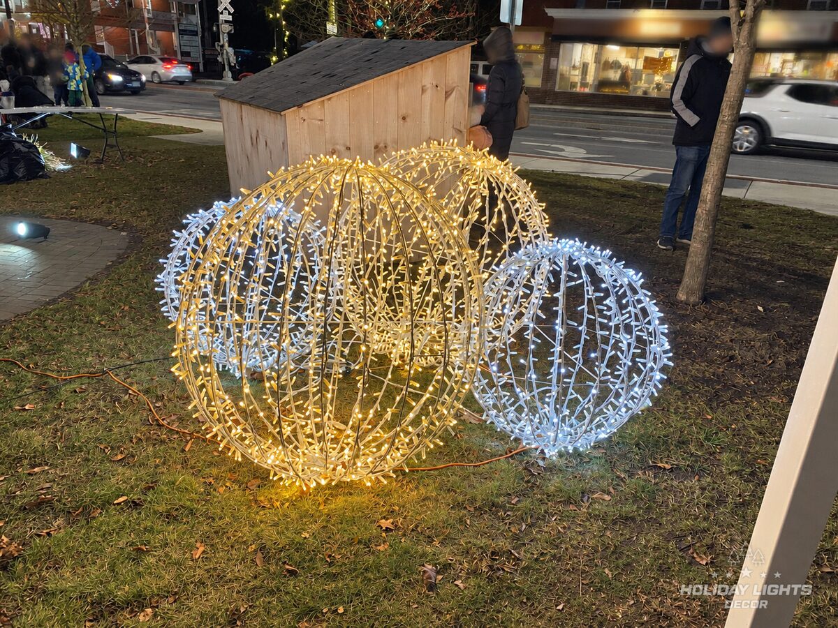 Cluster of illuminated spheres in warm and cool white with pedestrians behind them.