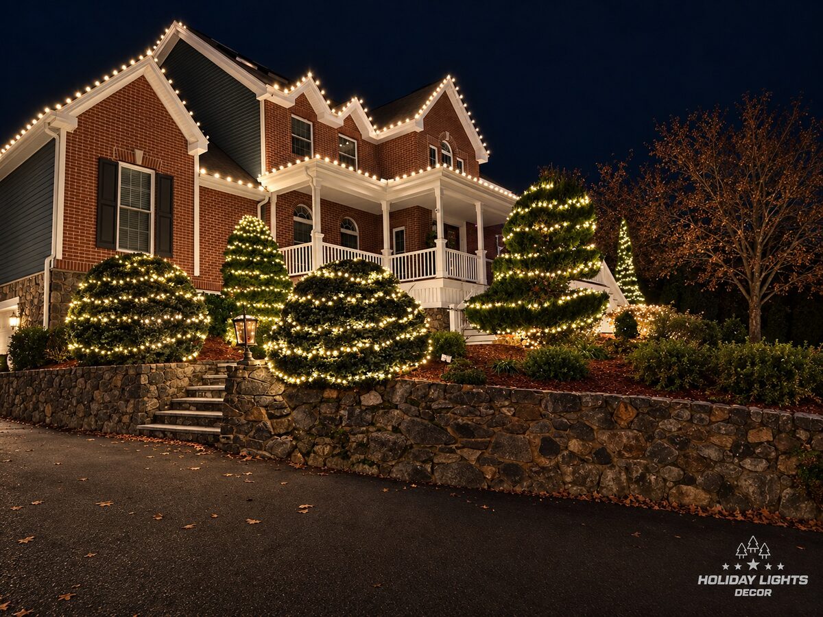 Closer view of the gables and porch of a Wakefield, MA brick home with warm white roofline lights and spiral-wrapped evergreens