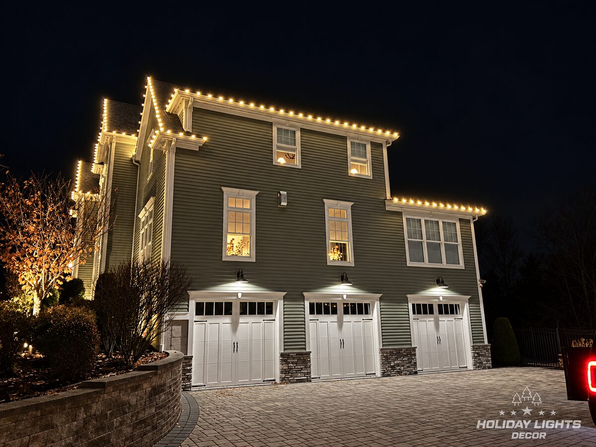 Warm-white roofline lights above a three-bay garage on a large two-story home.