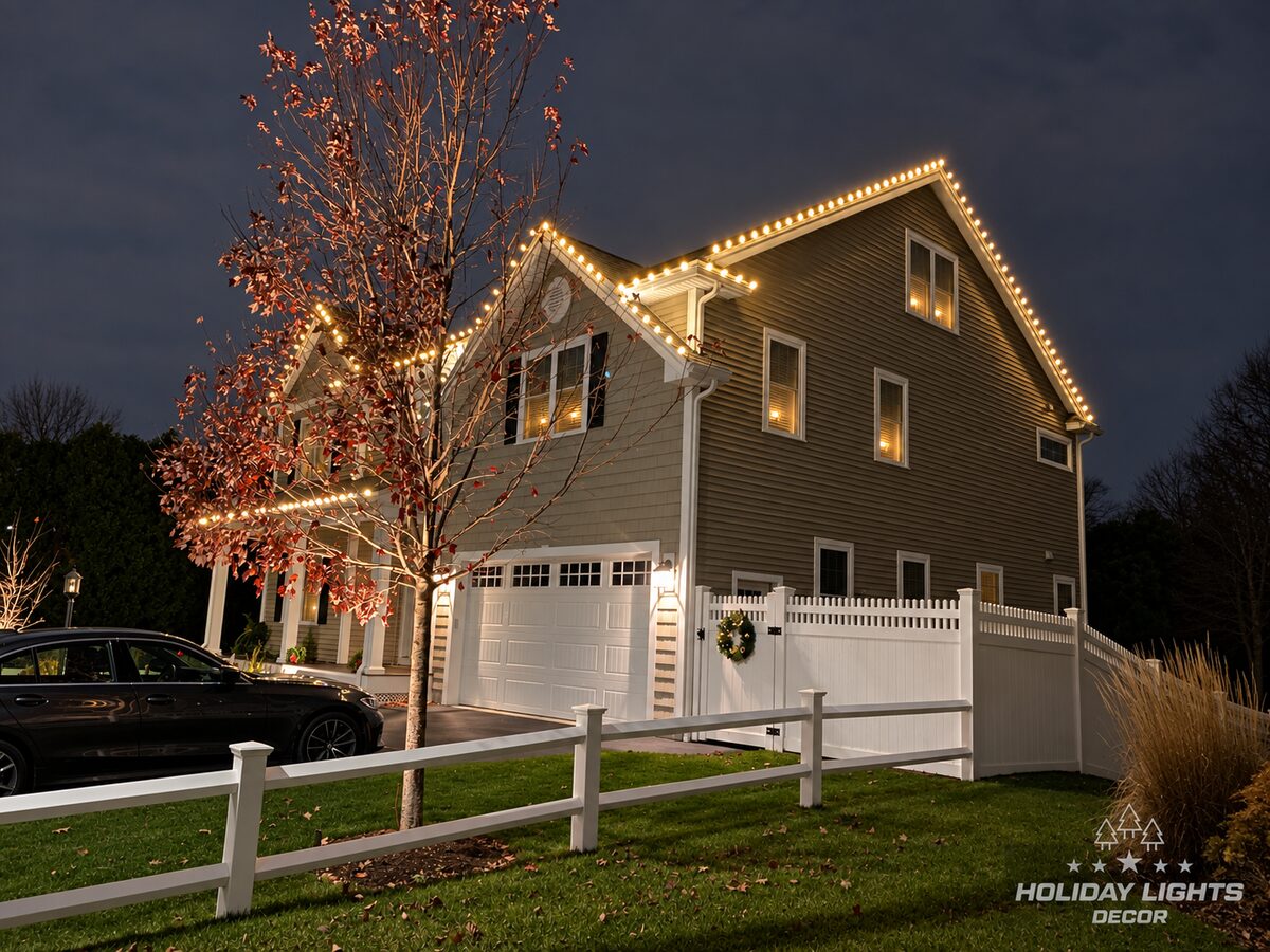 Night side view of a two-story home with warm-white lights tracing gables above a garage.